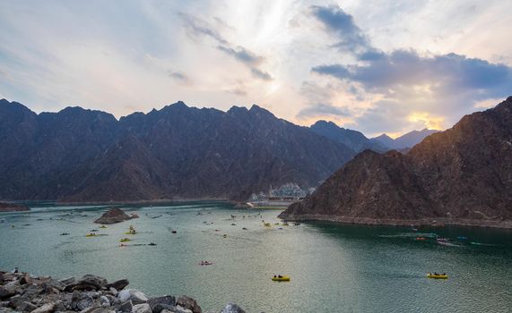 BEAUTIFUL AERIAL VIEW OF THE PADDLE BOATS, KAYAKS IN THE HATTA WATER DAM ON A CLOUDY DAY AT SUNSET TIME IN THE MOUNTAINS ENCLAVE REGION OF DUBAI, UNITED ARAB EMIRATES.