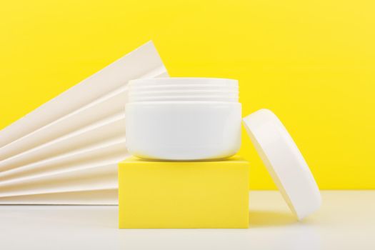 Close up of white opened jar on white table against yellow background decorated with white waver. Concept of summer skin or hair hair with sunblock. Face cream, mask, balm or scrub 
