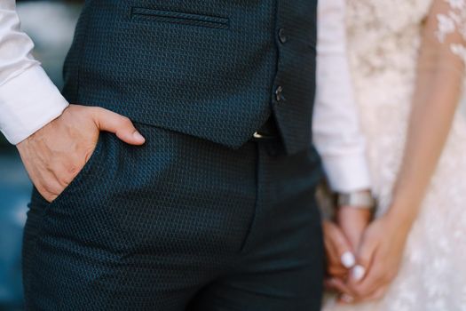 Groom in a navy suit holding his hand in his pocket. Bride is holding his other hand with hers.