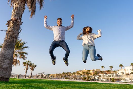 Happy people rejoice in the success of life jumping in air with open arms looking at the camera. Two young students in city nature enjoying freedom smiling for end of pandemic social restrictions