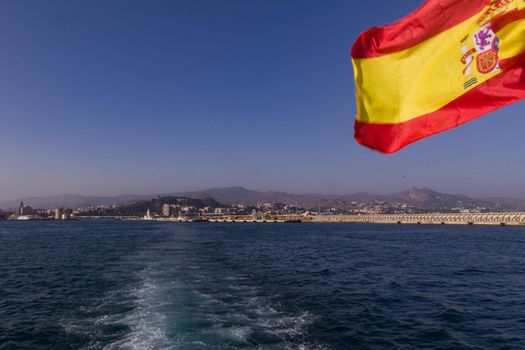 Wide-shot of the city of Malaga from the sea with a Spanish flag in the foreground