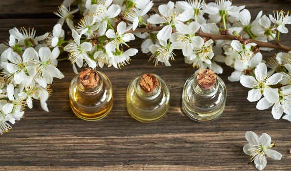 Three bottles of essential oil with white blossoms on a wooden background with copy space