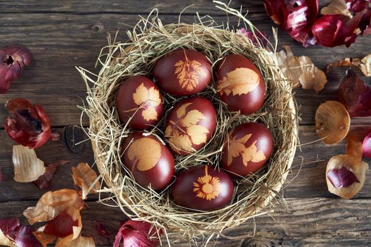Easter eggs dyed with onion peels with a pattern of fresh leaves in a wicker basket, top view