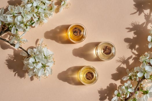 Three essential oil bottles on beige background with spring blossoms, top view