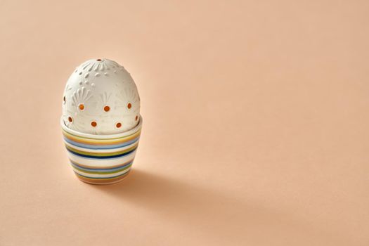 Blown out white Easter egg decorated with wax in a cup on orange pastel background with copy space