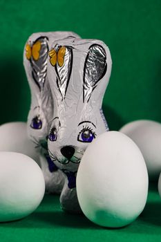 Wrapped chocolate Easter bunnies with white candy coated eggs on green