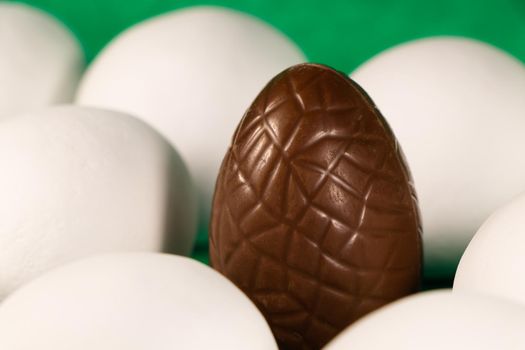 Brown chocolate Easter egg surrounded by white candy coated eggs