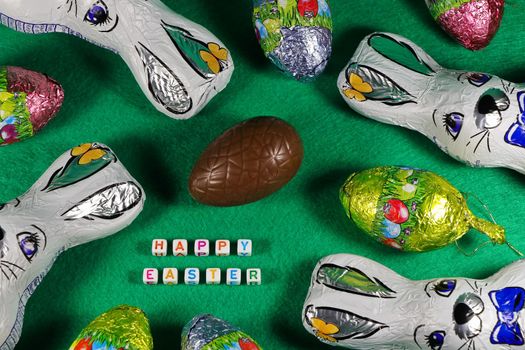 Happy Easter text with colorful wrapped chocolate Easter eggs and bunnies on green