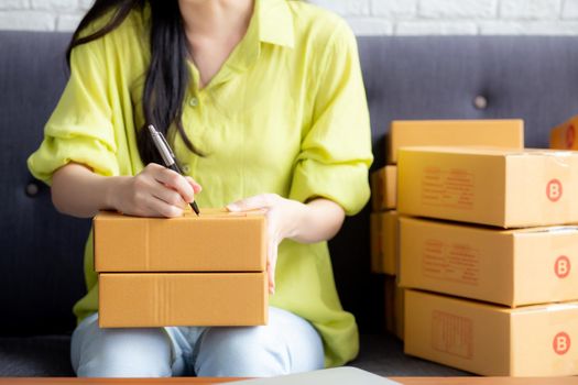 Closeup hand of young asian woman writing address on parcel box at home for delivery order to customer, shipping and logistic, merchant online and seller, business owner or SME, online shopping.