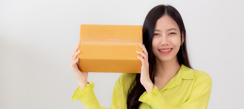 Young asian woman smiling and holding cardboard box with surprise at home, happy female carrying parcel box with excited, present and gift, packaging for deliver, online shopping store and service concept.