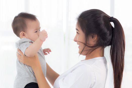 Young asian mother holding little baby girl together in the bedroom at home, mom carry child and care, woman and kid with carefree, toddler and parent, emotion and expression, family concept.