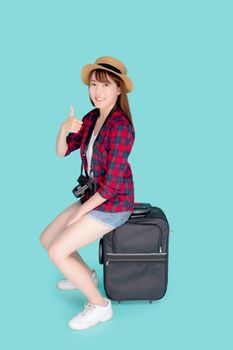 Beautiful portrait young asian woman sitting on luggage smile and travel summer trip for abroad in vacation, asia girl having camera gesture thumbs up on suitcase for journey with cheerful in holiday.