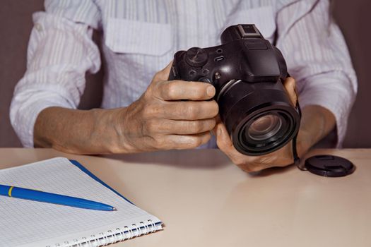 Camera is in hands of woman. Notebook and pen on light table.