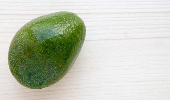 A ripe avocado sits on a light-colored chopping board.