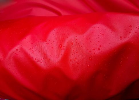 Large drops of water on a red textile with a waterproof effect. Water-repellent impregnation. Texture drops on the fabric.