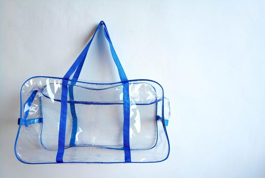 Plastic bag with blue handles hanging on a nail, on a white background.