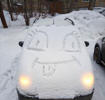 A car covered in snow, with a funny face on the hood. Winter fun.