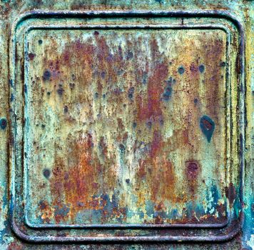 A heavily rusted metal plate with embossed parallel lines around the edge. The rusty metal is orange brown and turquoise in colour.