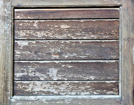 Panels of horizontal wood show heavy weathering with the surface layer peeling and missing in places. The panels are surrounded by a frame of similar weathered wood.