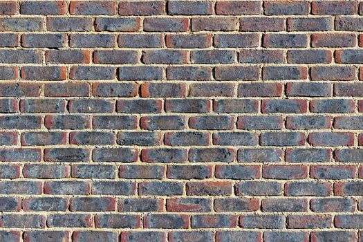 Photograph of a brick wall pattern. The bricks are red, blue and purple in colour with yellow mortar.