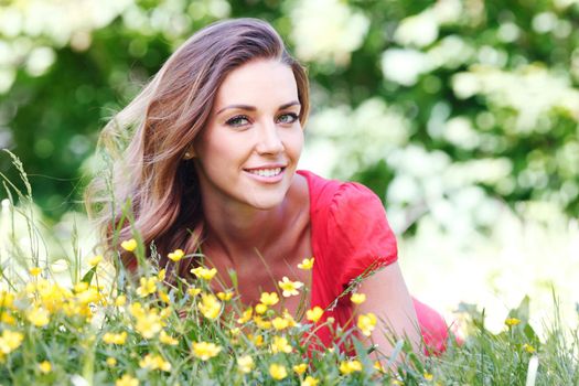 Beautiful young woman in red dress lying on grass