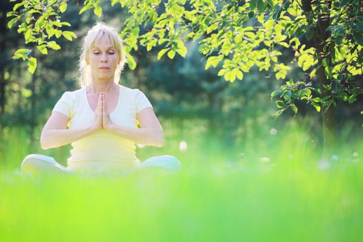 Beautiful mature woman in lotus yoga position in summer park