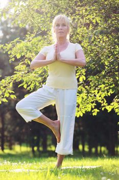 Beautiful mature woman practice yoga in summer park