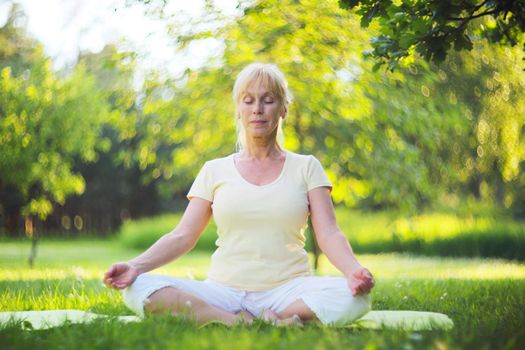 Beautiful mature woman in lotus yoga position in summer park