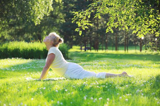 Beautiful mature woman practice yoga in summer park