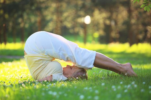 Beautiful mature woman practice yoga in summer park