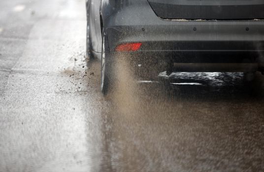 Dirt water splash flow from wheels of silver car moving fast in daylight city with selective focus. Car moving on dirty asphalt road after spring snow melting.