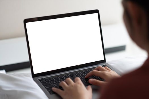 Woman working on laptop with white screen in bedroom at home.