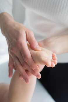 Mom gives her baby a leg and foot massage. Close-up. A satisfied baby lies on the massage table.