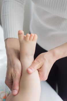 Mom gives her baby a leg and foot massage. Close-up. A satisfied baby lies on the massage table.