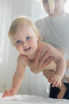 Mom does children's gymnastics for the baby, holding him by the chest. Close-up. Happy child is trying to climb.