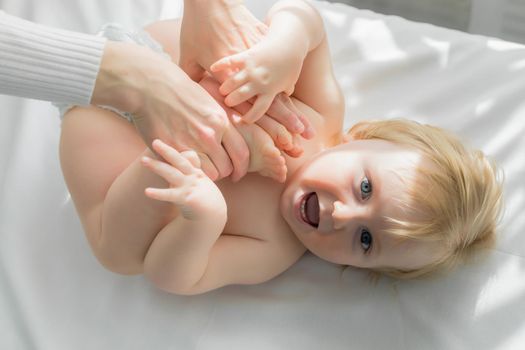 Mom does baby gymnastics for the baby's legs. Close-up. A happy child lies on his back.