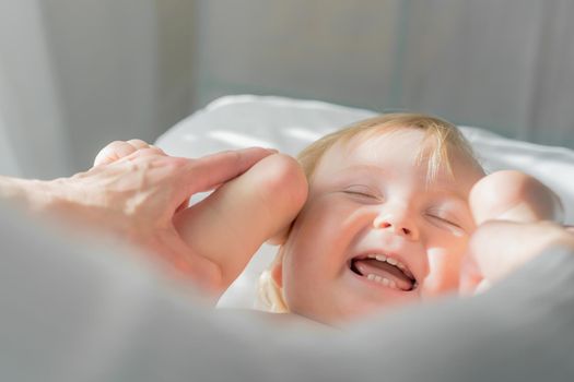 Mom does baby gymnastics for the baby's legs. Close-up. A happy child lies on his back.