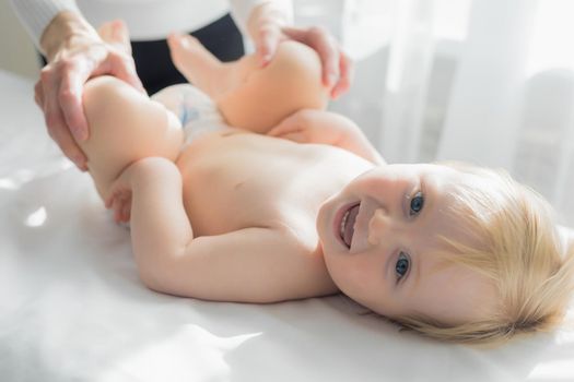 Mom does baby gymnastics for the baby's legs. Close-up. A happy child lies on his back.