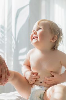 The kid rubs the tummy with cream before the massage. Close-up. The kid is sitting on the massage table.