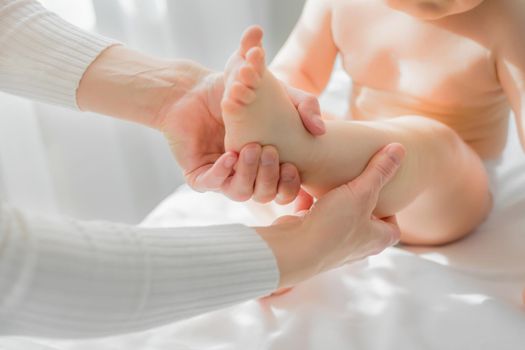 Mom gives her baby a leg and foot massage. Close-up. A satisfied baby is sitting on a massage table.