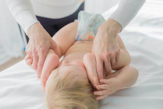 Mom does baby gymnastics for the baby's legs. Close-up. A happy child lies on his back.