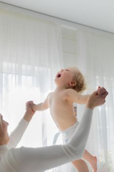 Mom throws the baby up, taking him by the hands, rejoicing and having fun.