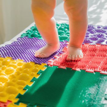 The kid walks barefoot on multi-colored massage rugs. Foot massage