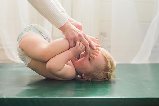 Mom does baby gymnastics for the baby's legs. Close-up. A happy child lies on his back.