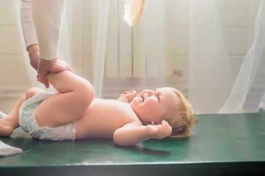 Mom does baby gymnastics for the baby's legs. Close-up. A happy child lies on his back.