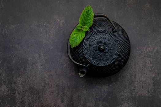 Black cast iron tea pot with herbal tea set up on dark stone background.