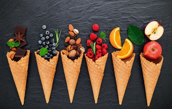 Various of ingredient for ice cream flavor in cones blueberry ,lime ,pistachio ,almond ,orange ,chocolate ,vanilla and coffee set up on dark stone background . Summer and Sweet menu concept.