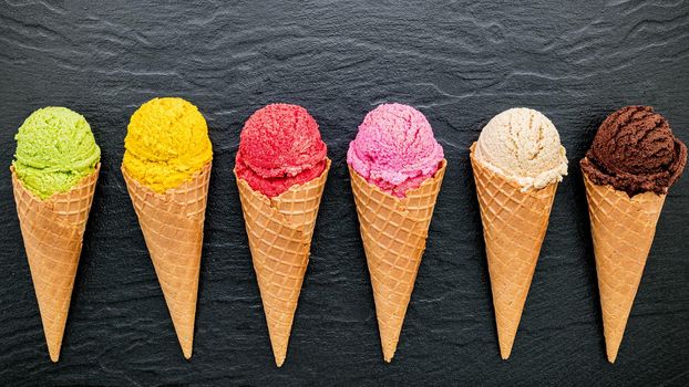 Various of ice cream flavor in cones blueberry ,lime ,pistachio ,almond ,orange ,chocolate ,vanilla and coffee set up on dark stone background . Summer and Sweet menu concept.