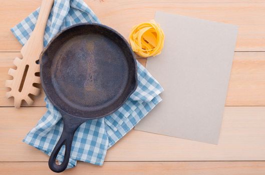 Food background for tasty Italian dishes with empty cast iron skillet and  pasta ladle on wooden background. Top view italian foods concept and menu design with copy space.