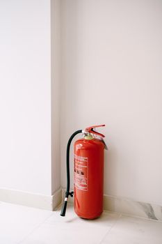 A red fire extinguisher on the floor in the corner against a white wall. High quality photo
